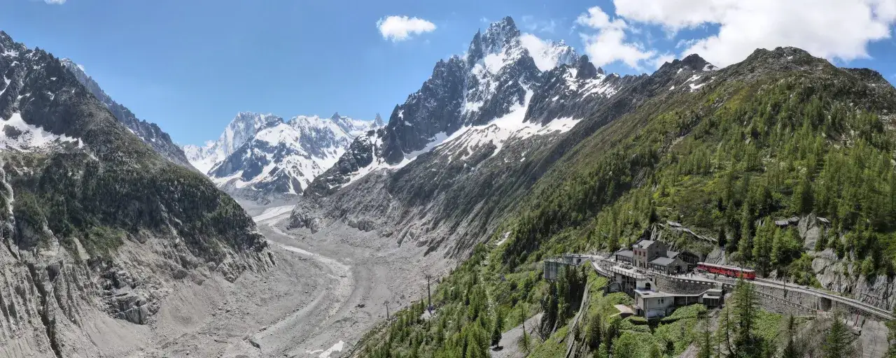 Magnifique panorama alpin pour un week-end à Chamonix. Un train rouge serpente sur les hauteurs, dominant un glacier et des montagnes enneigées.