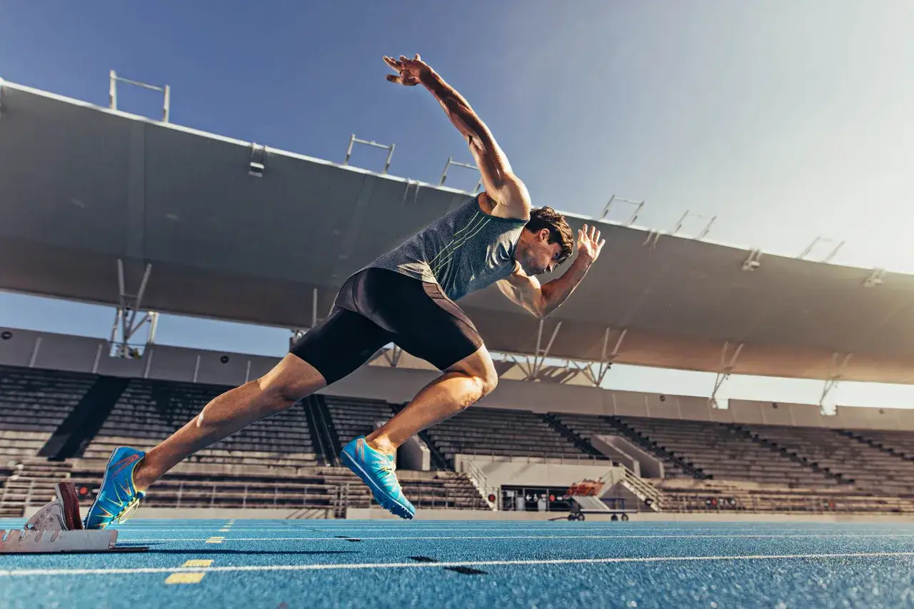 Athl&egrave;te en pleine action, d&eacute;part d'un entrainement sprint sur la piste bleue d'un stade.