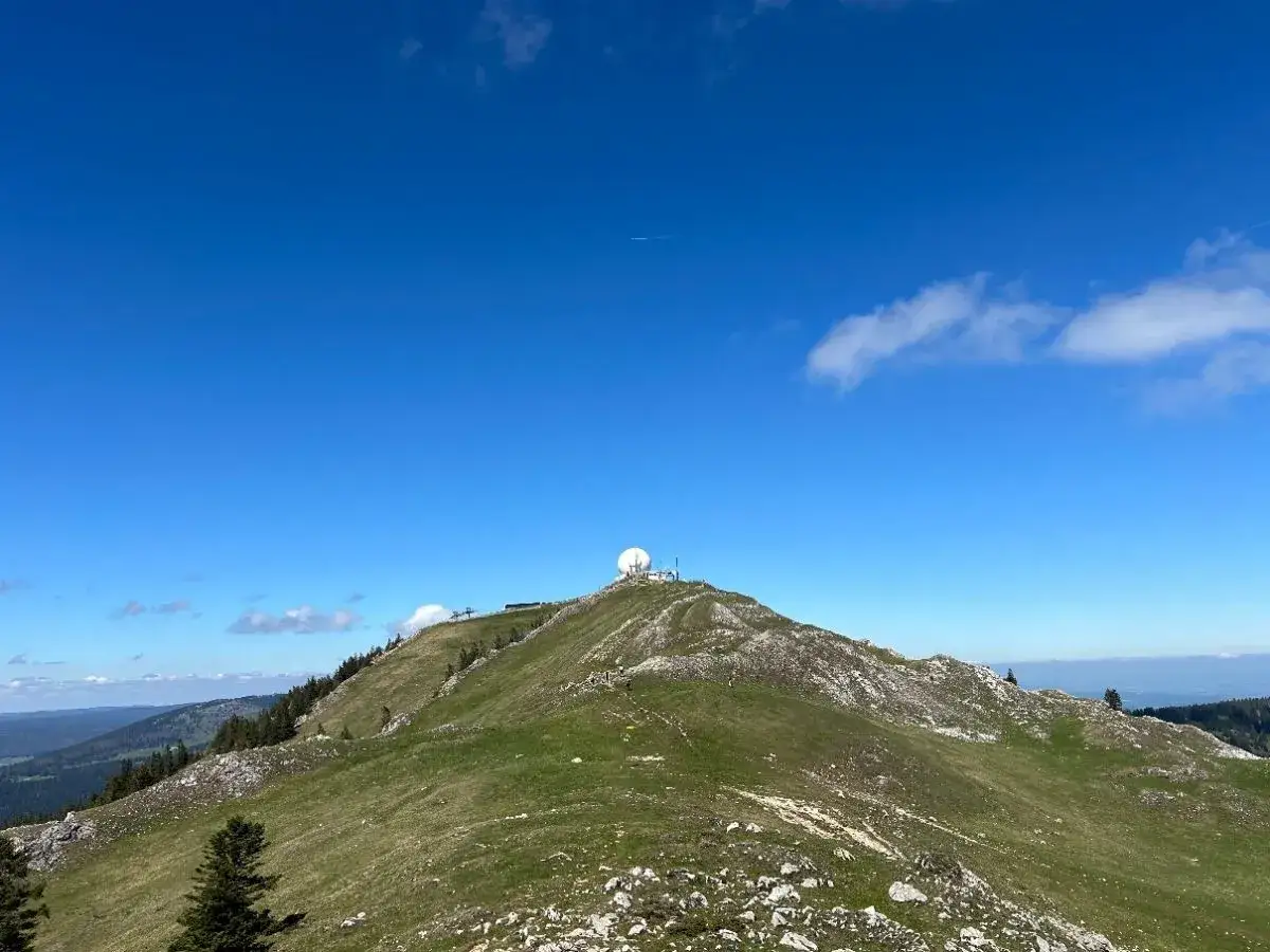 Vue panoramique d'une randonnée la dôle depuis les dappes. Le sommet rocheux et verdoyant est couronné d'une sphère blanche.