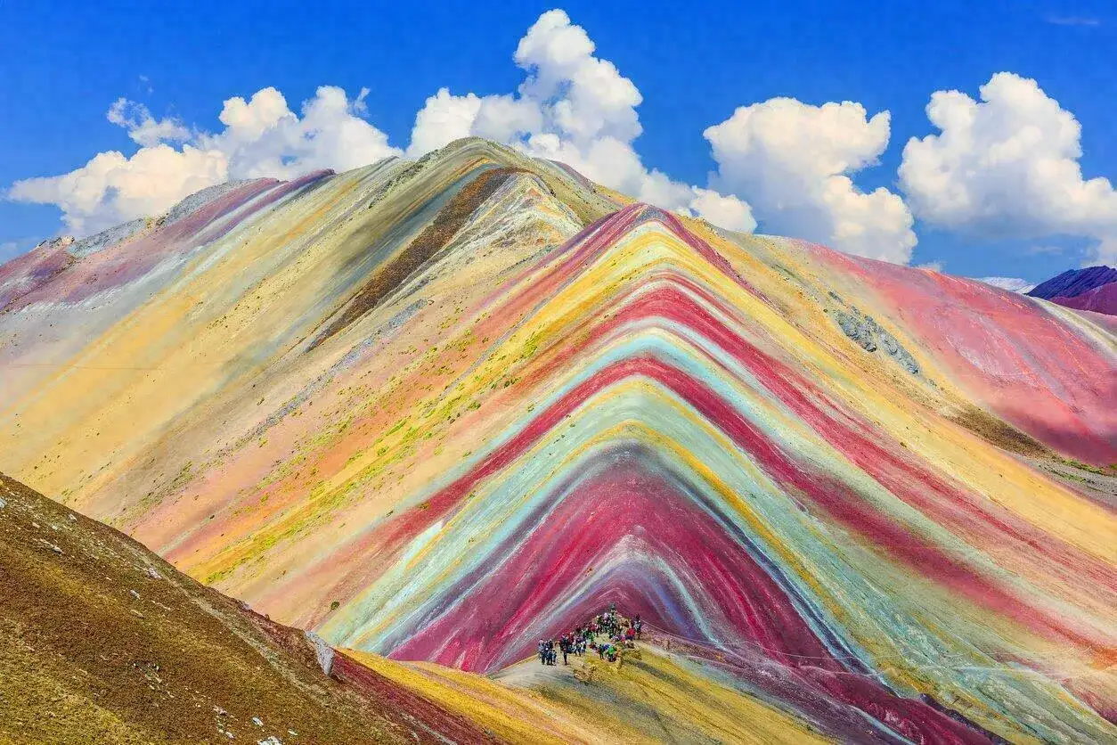 La montagne Vinicunca, aux couleurs vives, d&eacute;voile ses strates min&eacute;rales sous un ciel bleu parsem&eacute; de nuages.