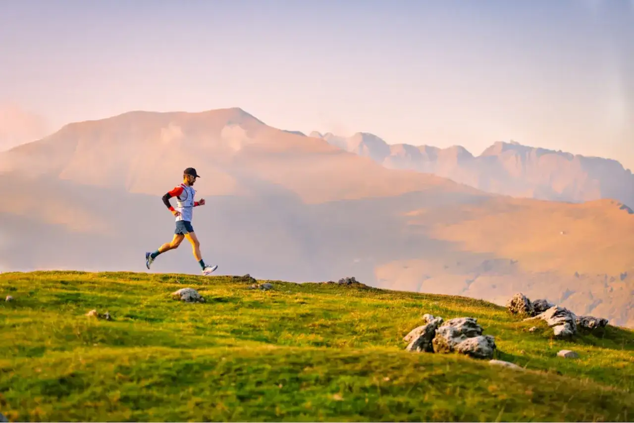 Un coureur en plein effort sur une cr&ecirc;te herbeuse, paysage montagneux en arri&egrave;re-plan. Il participe au championnat du monde de trail long.
