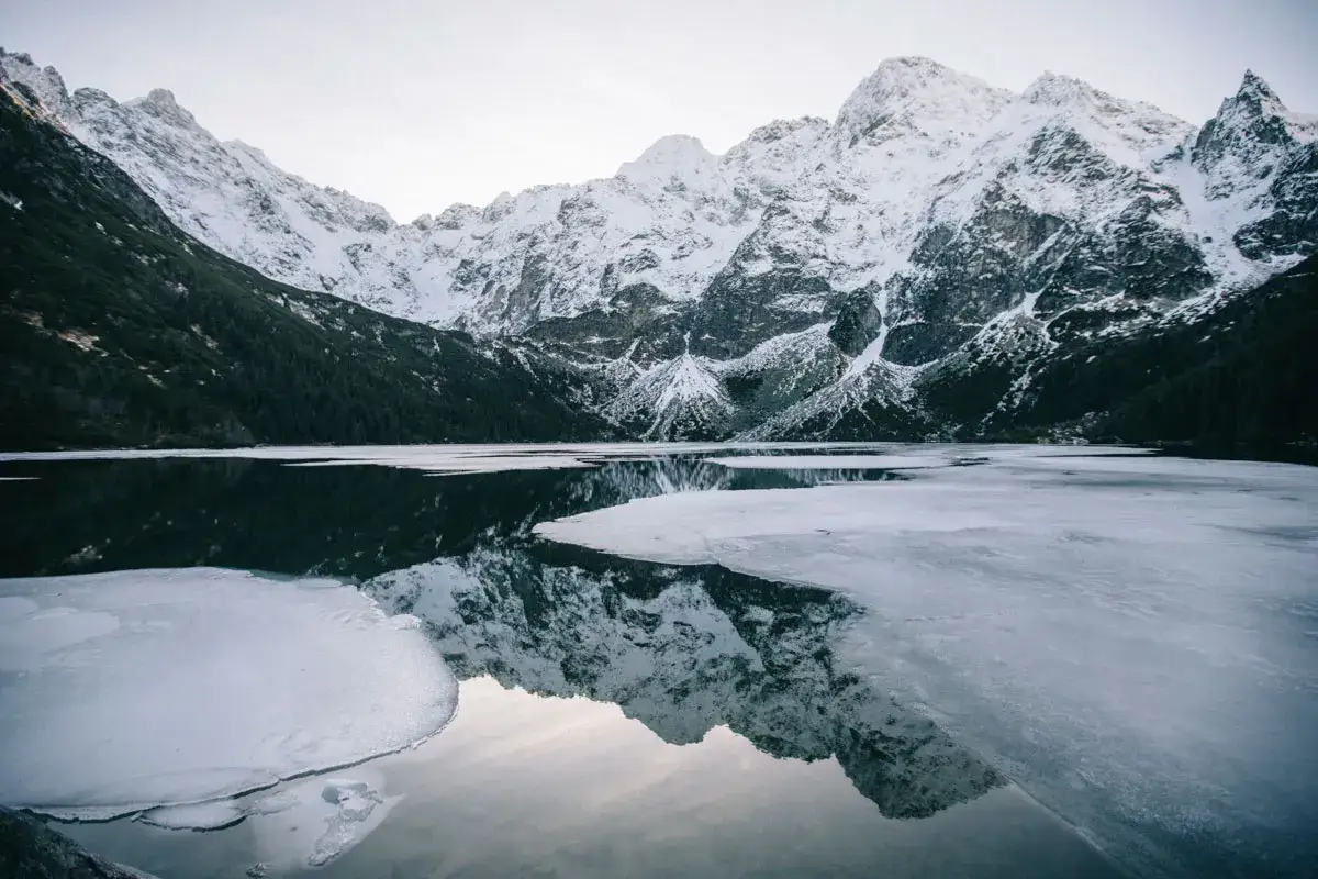 Lac gel&eacute; et montagnes enneig&eacute;es dans les Tatras en Pologne, refl&eacute;tant la beaut&eacute; hivernale.