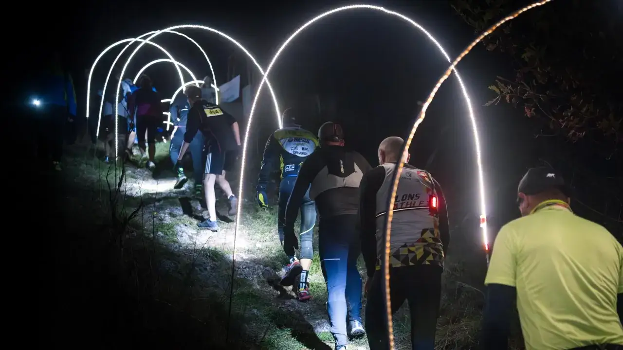 Coureurs dans un dark trail à Orgelet, éclairés par des arches lumineuses sur un sentier nocturne.