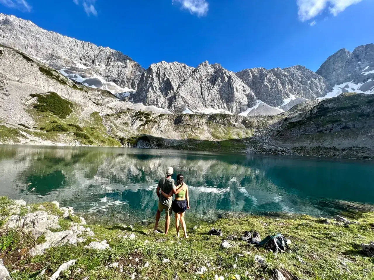 Couple admirant un lac turquoise lors d'un trek en Autriche, avec des montagnes majestueuses en arri&egrave;re-plan.