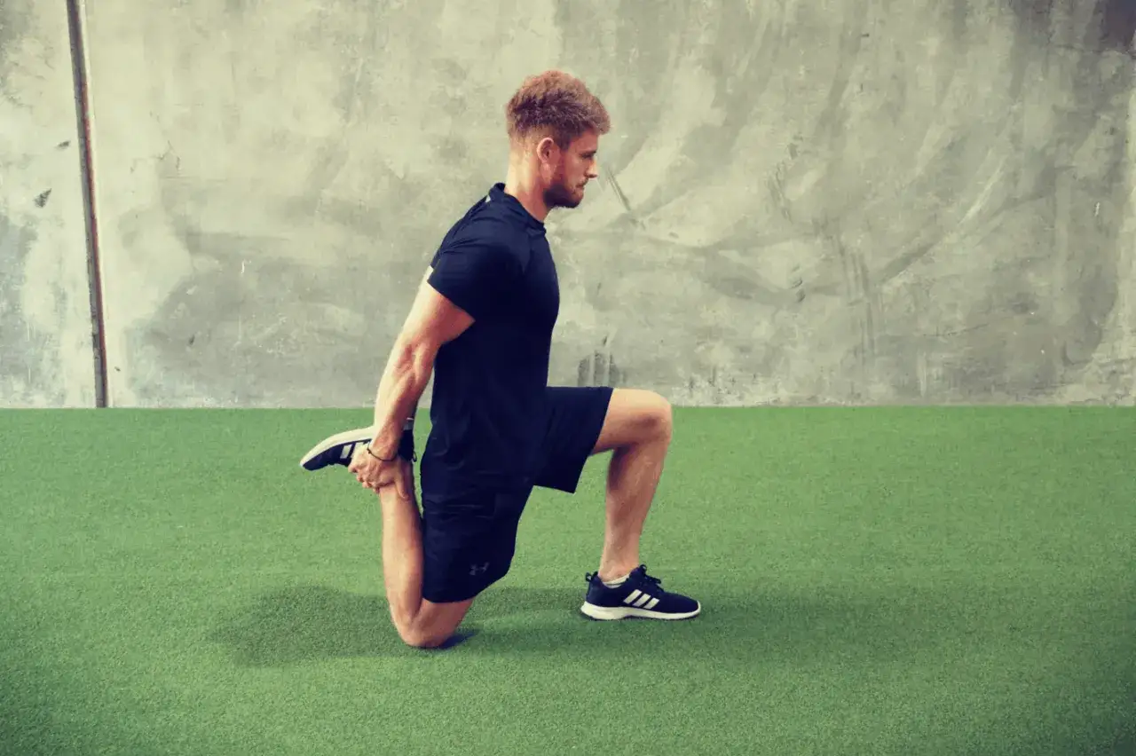 Homme en tenue de sport, genou au sol, effectuant un &eacute;tirement de la cuisse avec une jambe en l'air.
