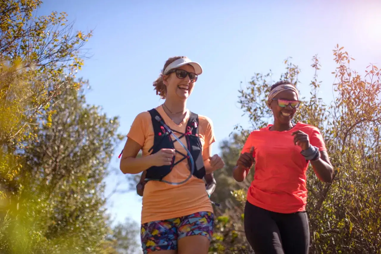 Deux femmes souriantes s'entra&icirc;nent en plein air, profitant de la nature. Leur m&eacute;thode norv&eacute;gienne course les pousse &agrave; se d&eacute;passer.