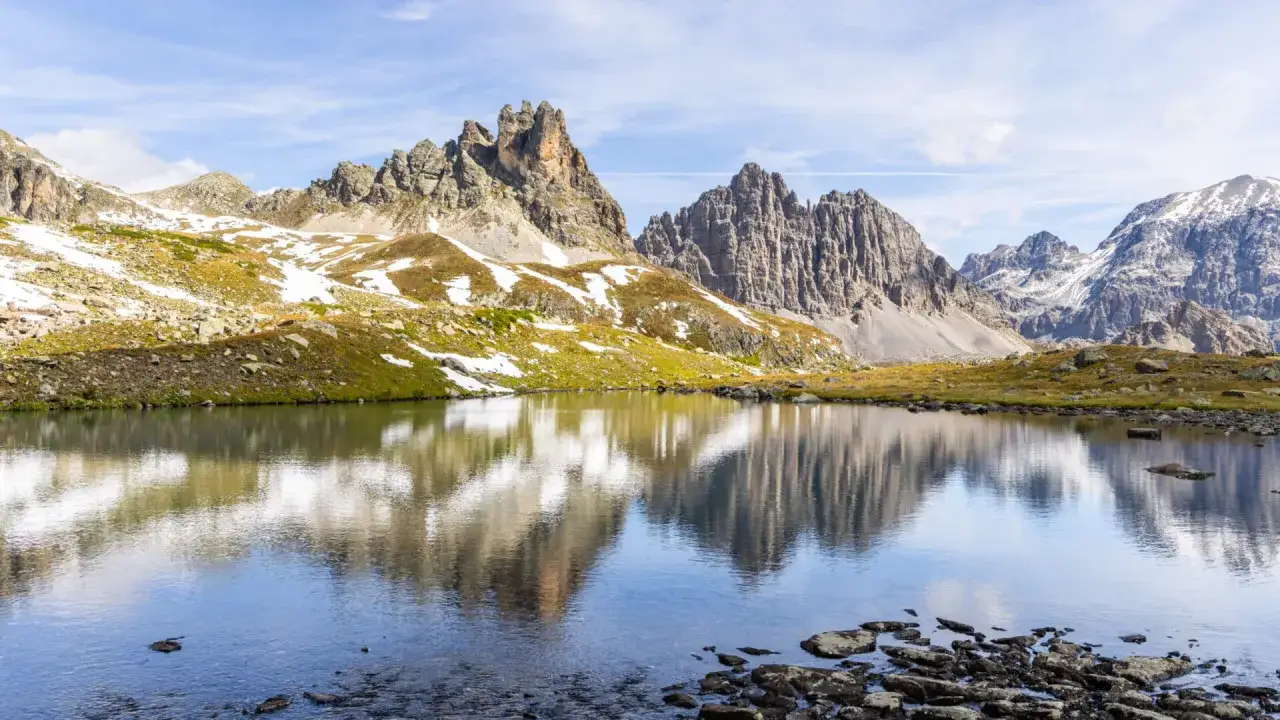 Reflets parfaits des montagnes escarp&eacute;es dans un lac paisible, la vall&eacute;e de la Clar&eacute;e en &eacute;t&eacute;, avec des touches de neige sur les pentes verdoyantes.