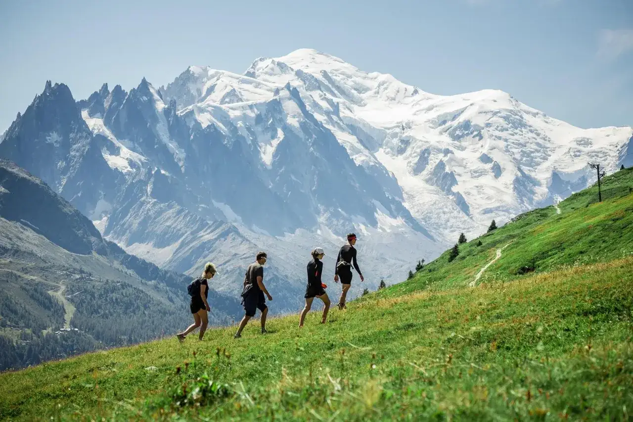 Quatre randonneurs gravissent une pente verdoyante, le Mont-Blanc enneig&eacute; en toile de fond. Une belle randonn&eacute;e &agrave; Chamonix.