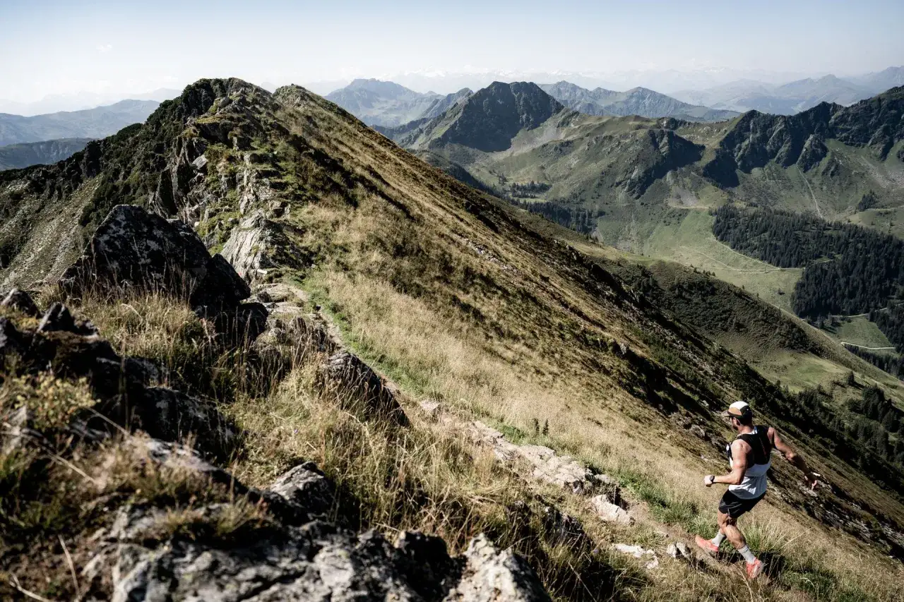 Un coureur affronte le sentier escarpé du kat100 by utmb, dominant un paysage montagneux spectaculaire.