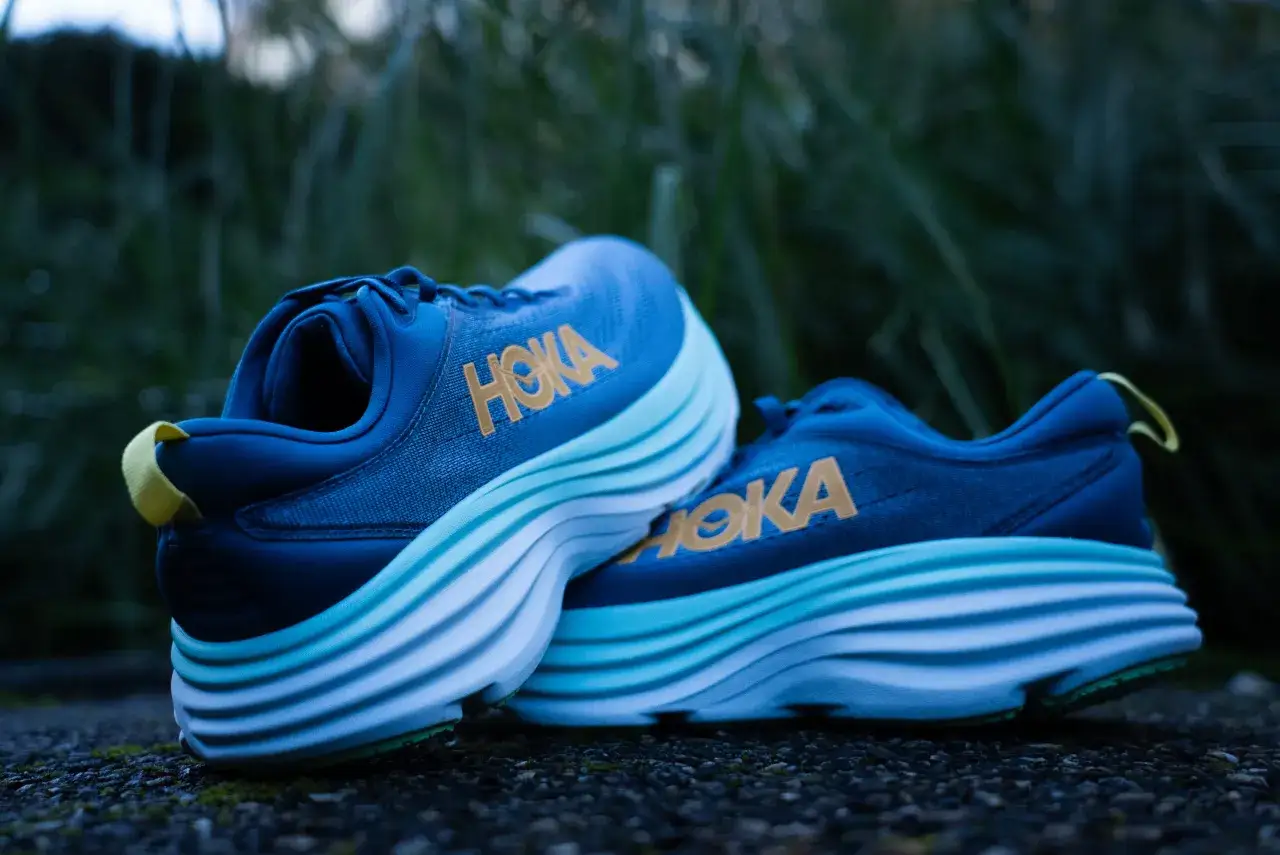 Paire de chaussures de course Hoka bleues avec semelles &eacute;paisses d&eacute;grad&eacute;es bleu clair et blanc. Le logo Hoka dor&eacute; est visible. Le drop 8mm est id&eacute;al pour le confort.