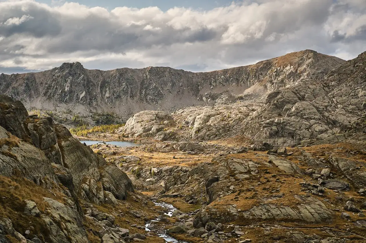 Paysage rocheux et herbeux du Mercantour, avec un lac et un ruisseau. Parfait pour une randonn&eacute;e mercantour 3 jours.
