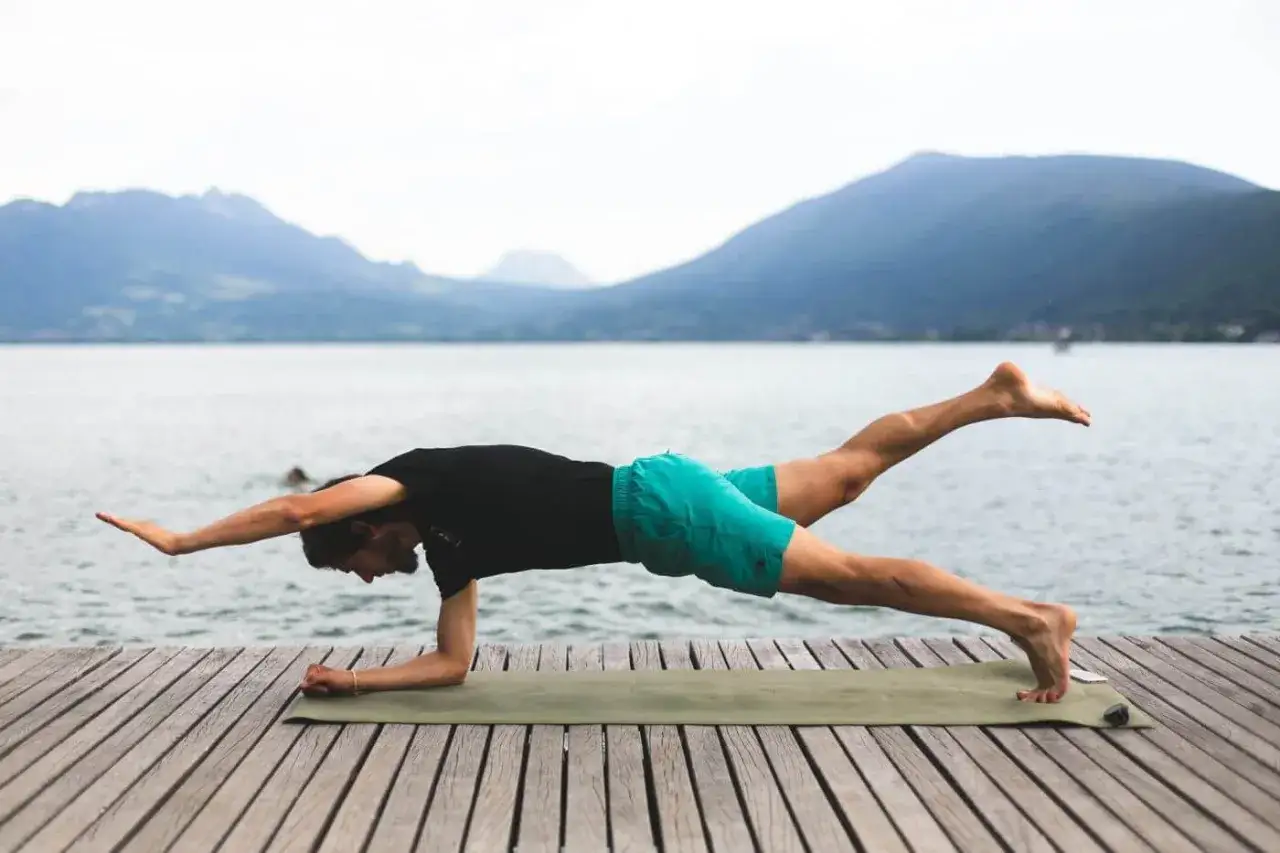 Un homme en planche lat&eacute;rale sur un tapis, parfait pour le renforcement musculaire trail. Paysage lacustre et montagneux en arri&egrave;re-plan.