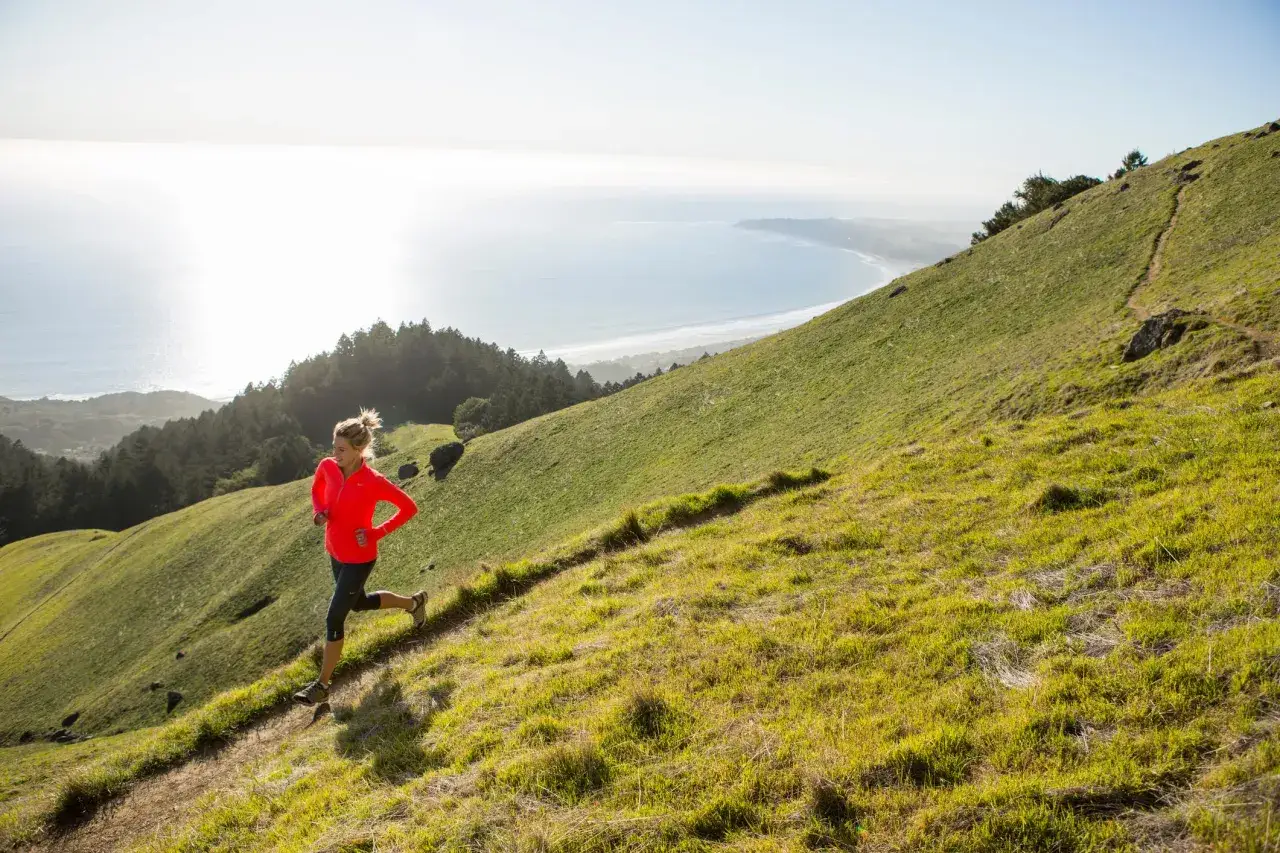 Femme courant sur une colline verdoyante, profitant d'un sport aérobie avec vue sur l'océan.