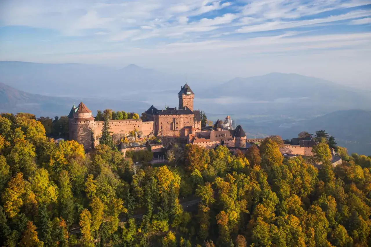 Les 3 ch&acirc;teaux de Ribeauvill&eacute;, perch&eacute;s sur une colline bois&eacute;e aux couleurs d'automne, dominent le paysage alsacien sous un ciel bleu et nuageux.