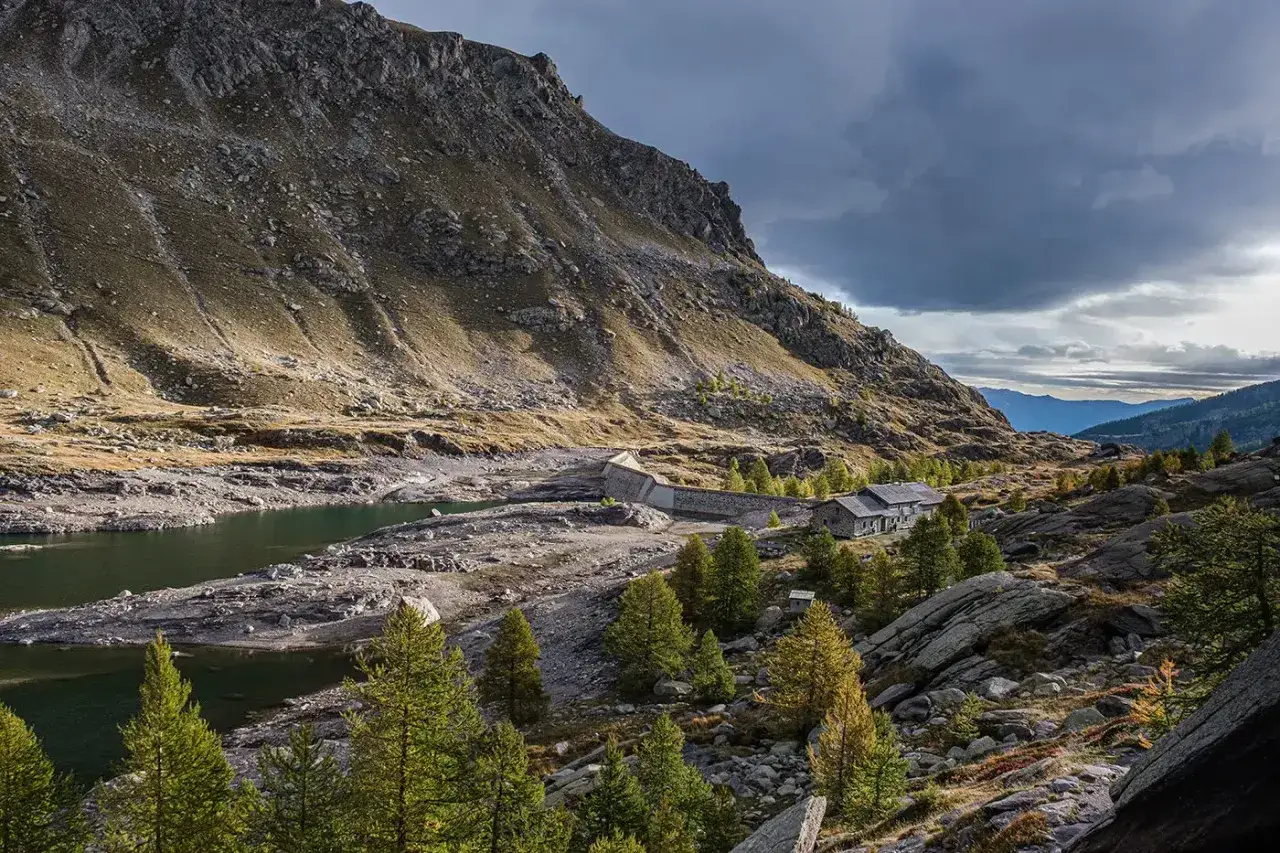 Vue d'un lac et d'un refuge de montagne, parfait pour une randonnée vallée des merveilles 2 jours. Le soleil perce les nuages sur la pente rocheuse.