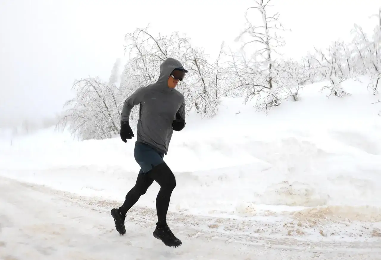 Un coureur déterminé affronte le froid et la neige lors d'un running hivernal, entouré d'arbres givrés.