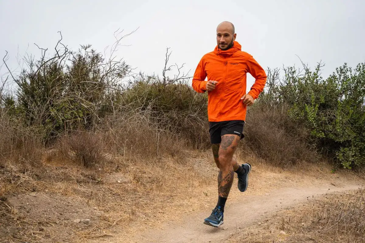 Un homme court sur un sentier, portant une veste pour courir l'hiver orange vif.
