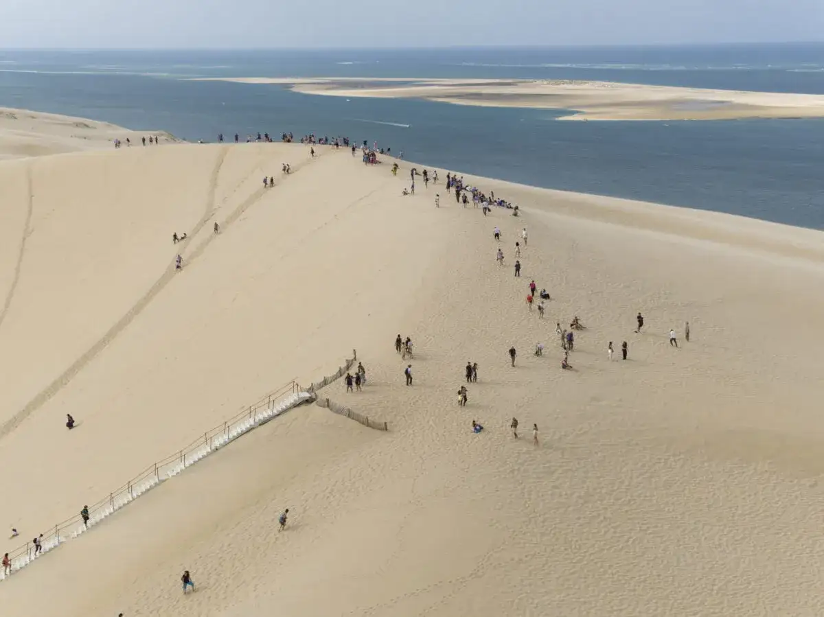 La dune du Pilat, immense étendue de sable, accueille des visiteurs qui escaladent ses pentes douces, offrant une vue imprenable sur l'océan.