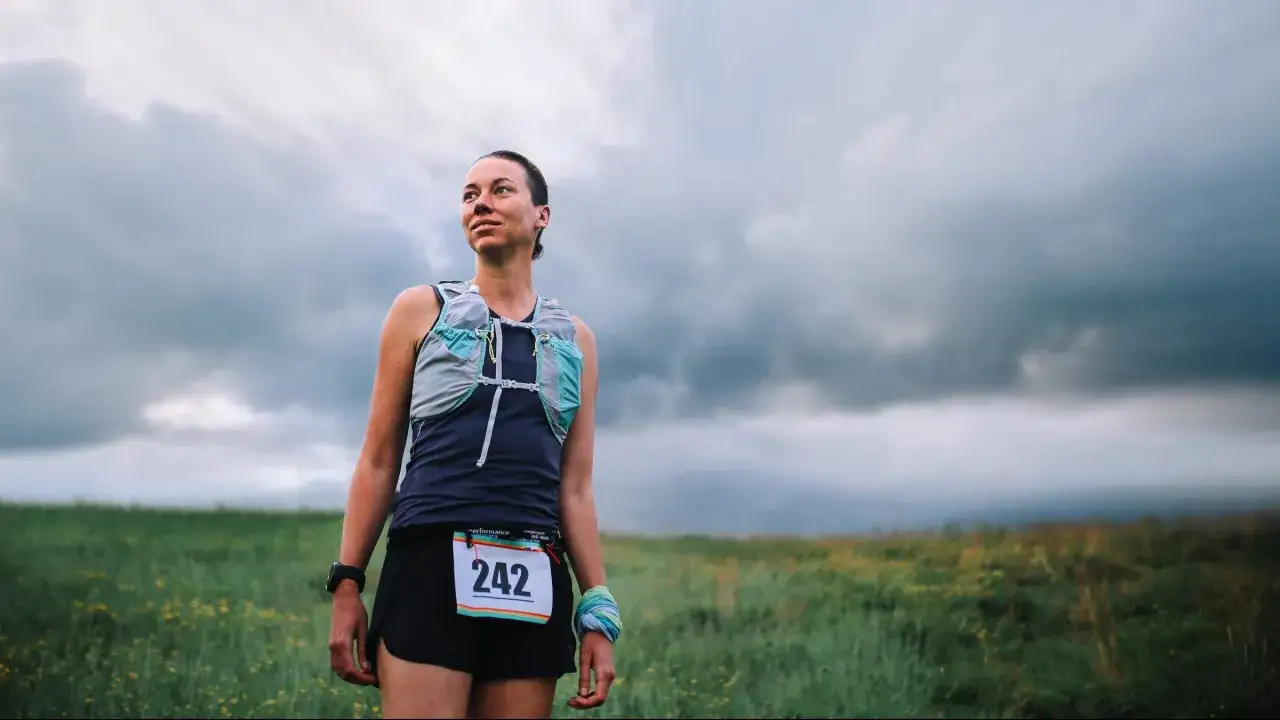Athlète prête pour son plan entrainement trail 50 km, sous un ciel menaçant. Elle porte un dossard 242.