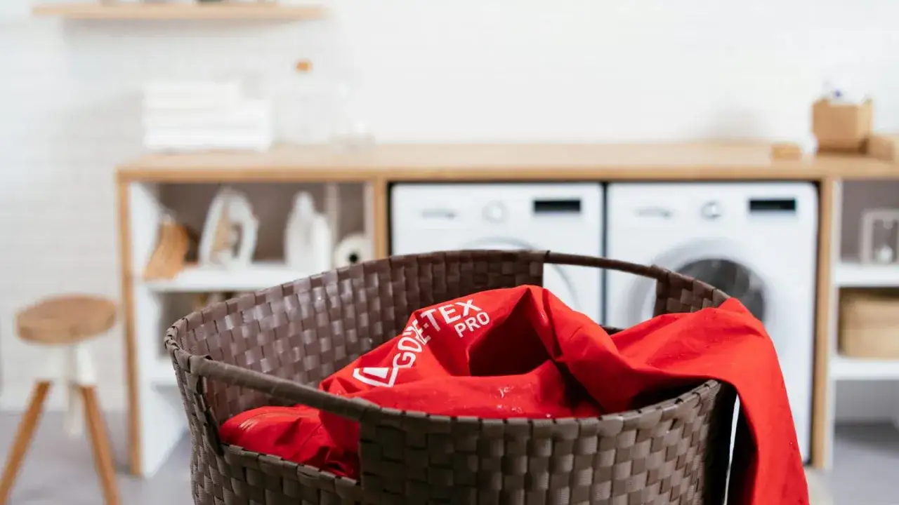 Veste rouge GORE-TEX PRO dans un panier &agrave; linge, pr&ecirc;te pour le lavage.