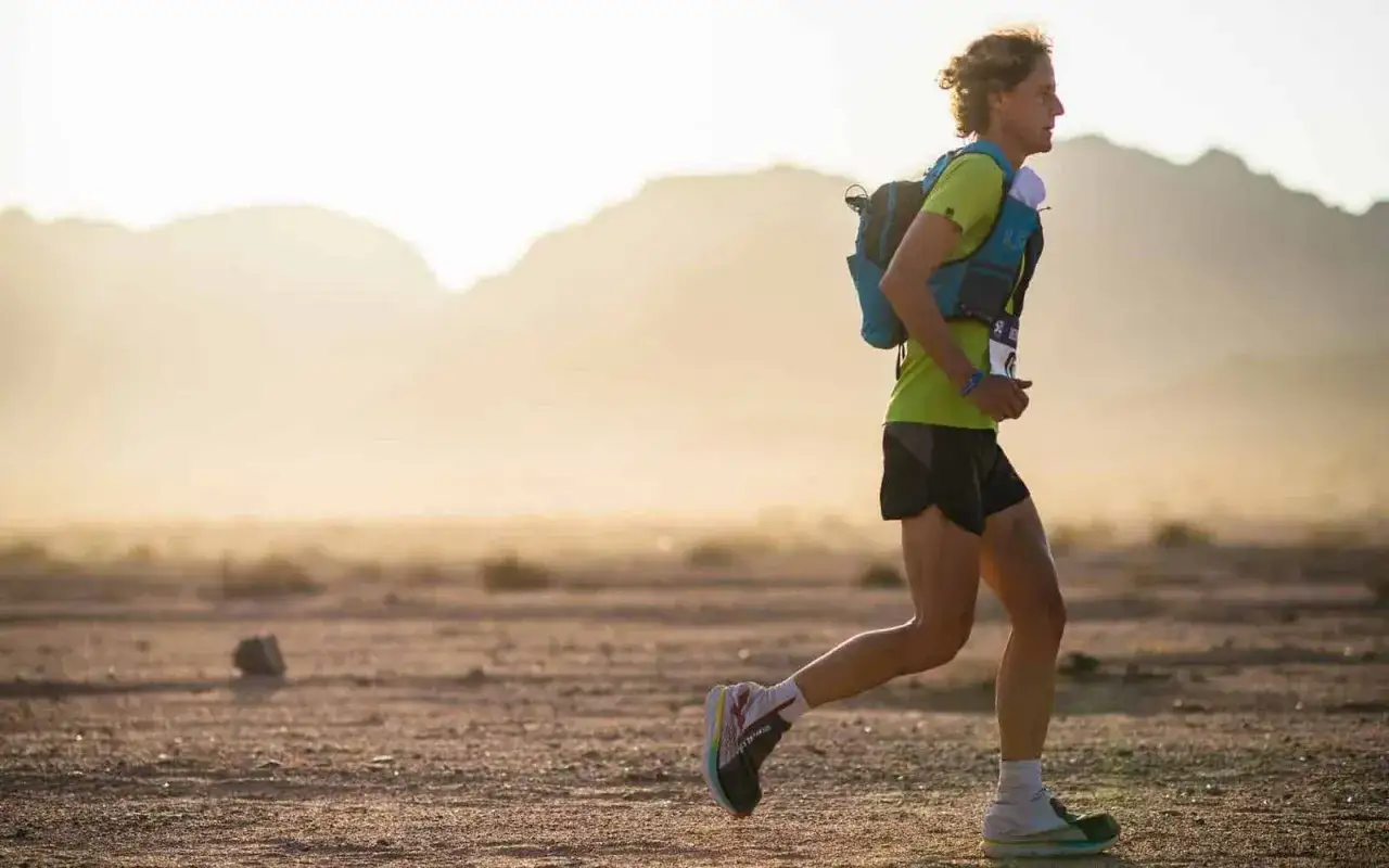 Coureur en plein effort, sac &agrave; dos et tenue de sport adapt&eacute;s &agrave; l'&eacute;quipement ultra trail dans un paysage d&eacute;sertique.
