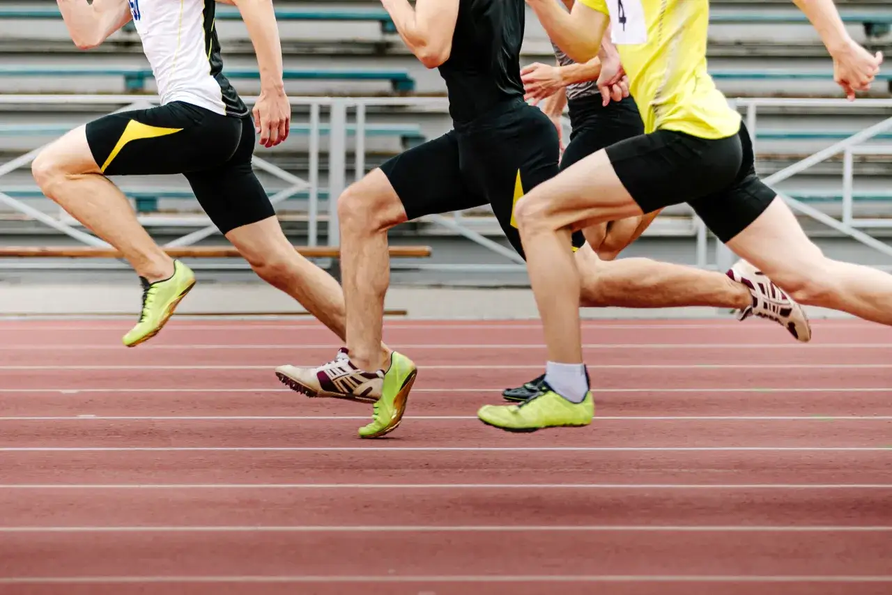 Trois athl&egrave;tes en pleine course sur une piste d'athl&eacute;tisme. Leurs jambes muscl&eacute;es et leurs pointes de course t&eacute;moignent d'un renfo course &agrave; pied intense.