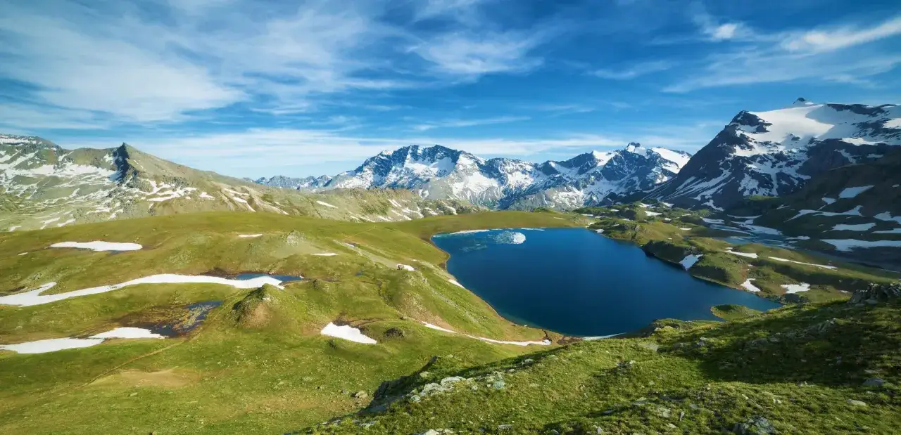 Un lac bleu profond reflète le ciel azur, entouré de montagnes enneigées et de prairies verdoyantes. Un paysage d'une beauté à couper le souffle, un véritable grand paradis.