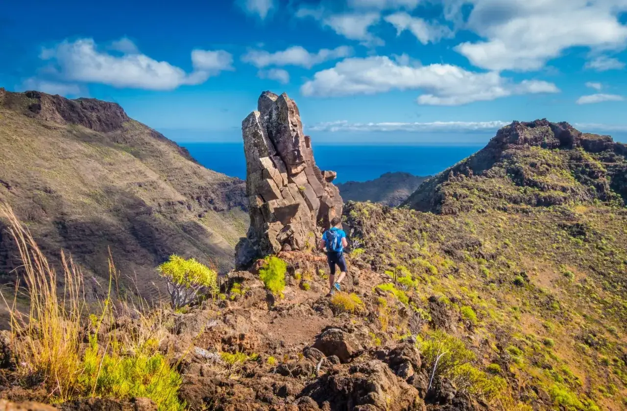 Un randonneur explore un sentier escarp&eacute; &agrave; Tenerife, dominant l'oc&eacute;an bleu sous un ciel &eacute;clatant.