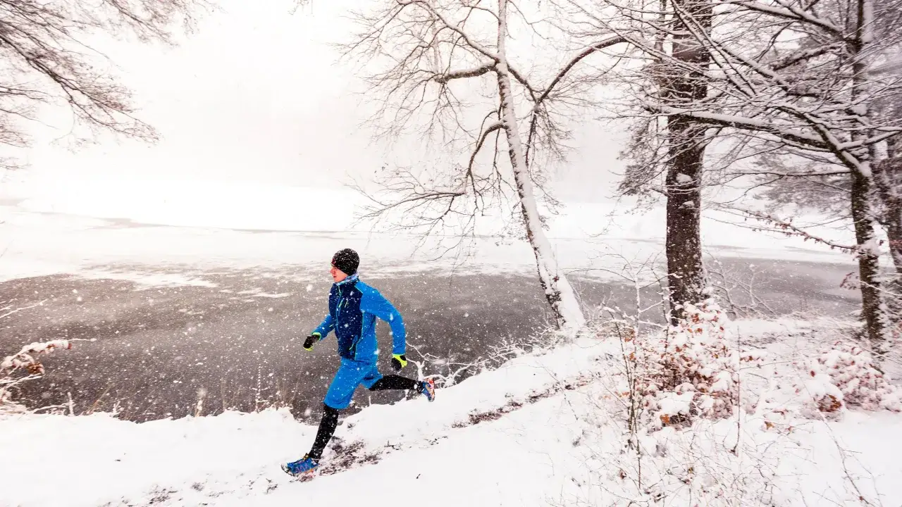 Un homme court sous la neige pr&egrave;s d'un lac gel&eacute;, entour&eacute; d'arbres d&eacute;nud&eacute;s.