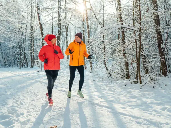 Un couple profite de l'air frais en courant sous la neige dans une forêt enneigée.