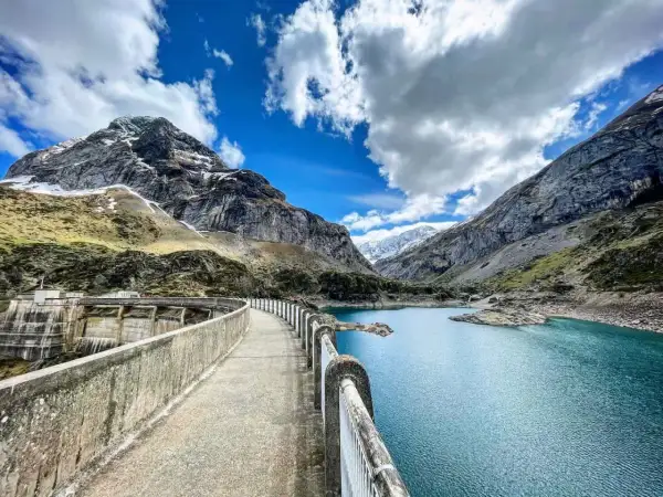 Le cirque de Gavarnie lac, un barrage imposant domine un lac bleu turquoise, entouré de montagnes majestueuses sous un ciel nuageux.