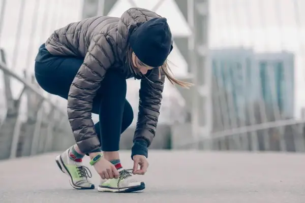 Une femme en tenue de running hiver attache ses lacets sur un pont.