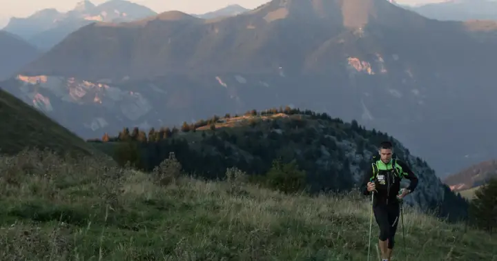 Un coureur en plein effort, bâtons en main, sur un sentier de montagne. Un aperçu de son plan d'entraînement UTMB.
